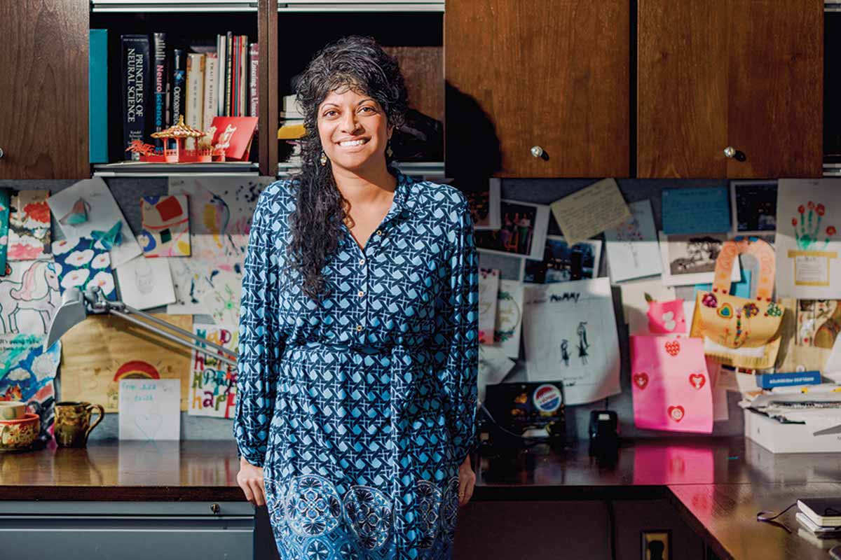 Rajasethupathy leans against their desk with books and colorful artwork in the background