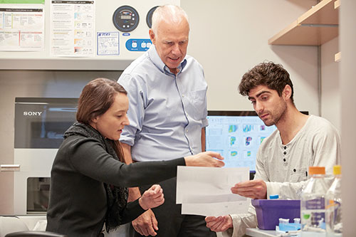 A research scientist with two graduate fellows in a lab.